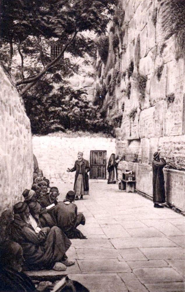 אנשים ונשים יושבים ועומדים בתפילה מול אבני הכותל המערבי