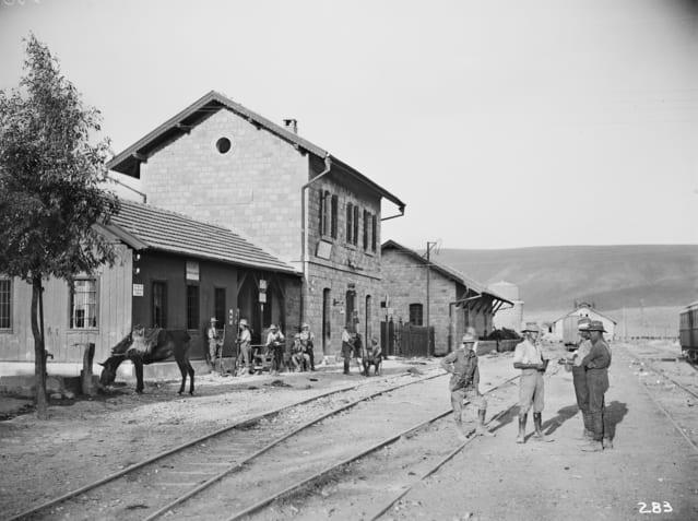 בנין תחנת רכבת ולפניו מסילות ואנשים